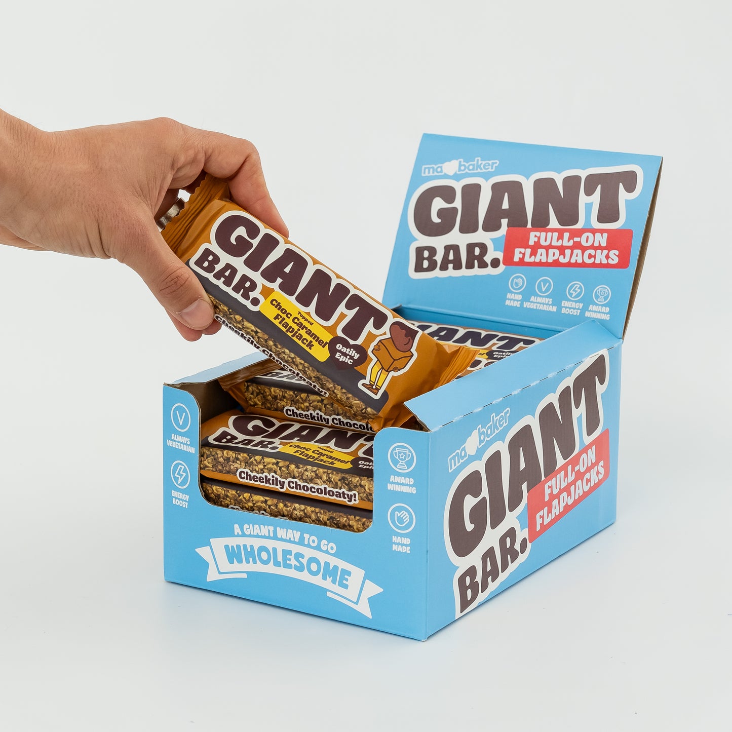 A hand taking a Topped Choc Caramel Giant Bar out of a box of Giant Bars