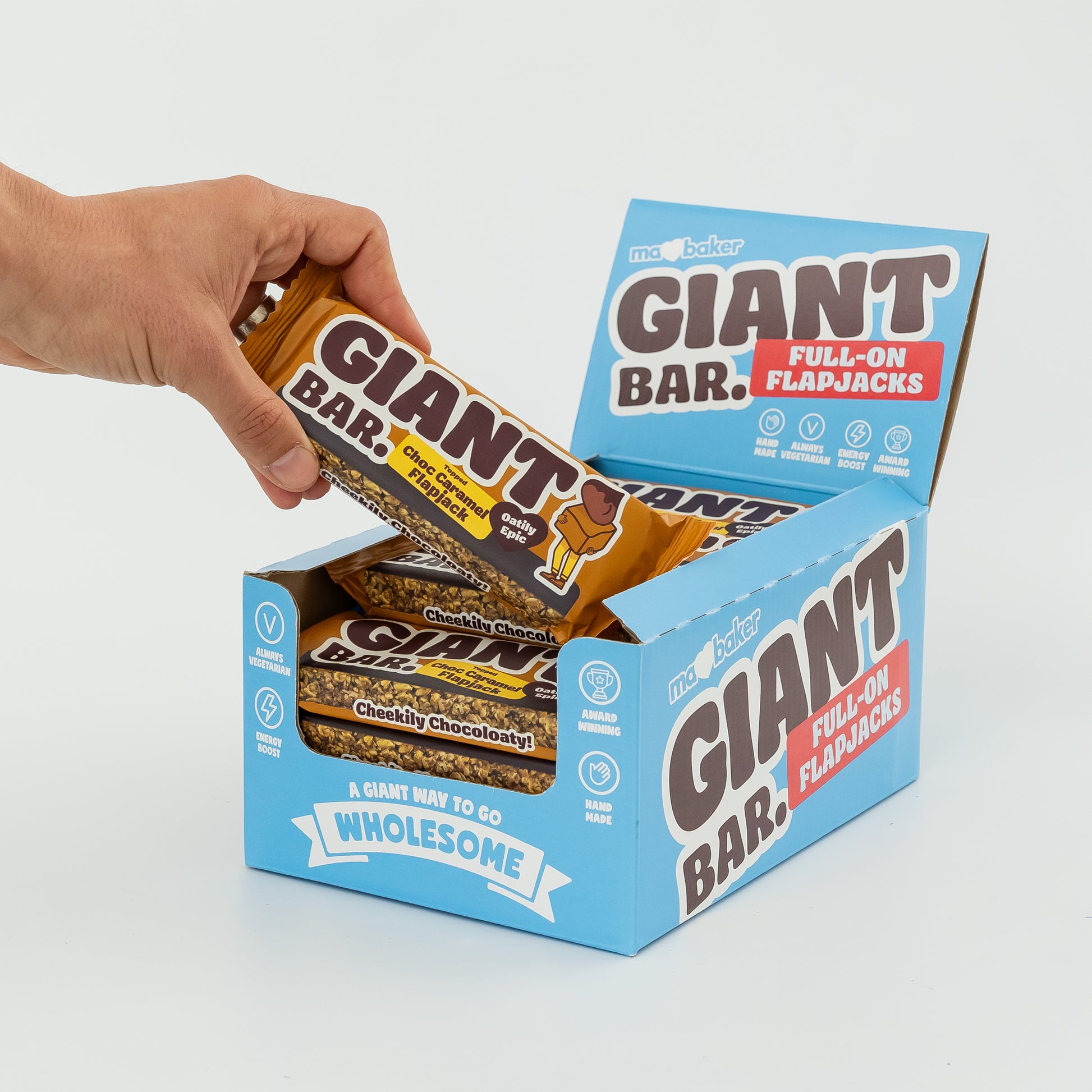 A hand taking a Topped Choc Caramel Giant Bar out of a box of Giant Bars
